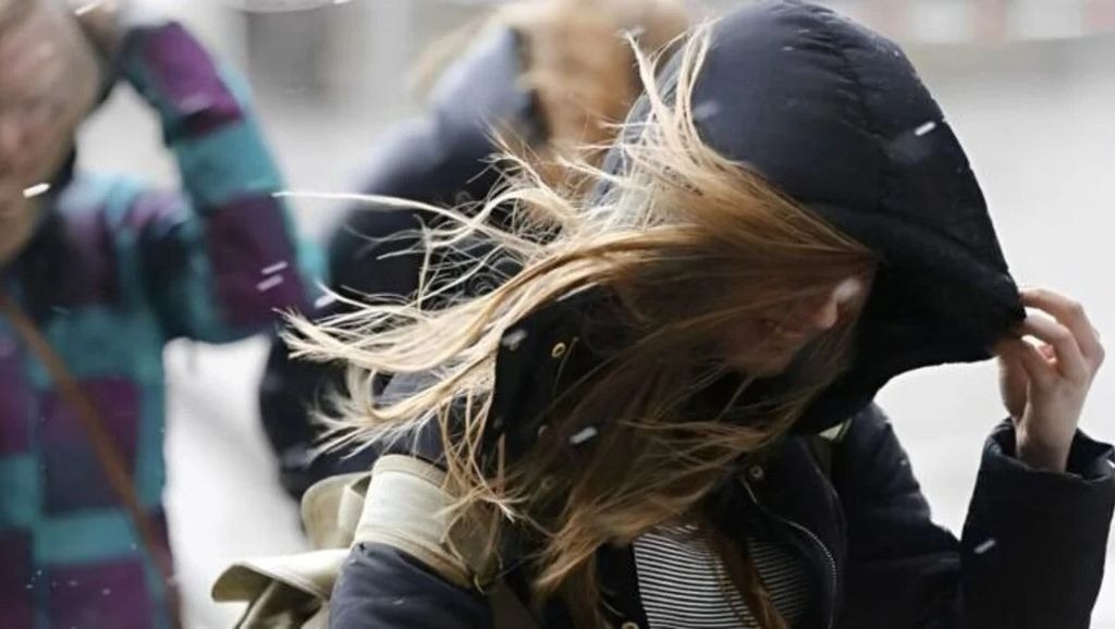 Mujer se protege del viento y el graupel sosteniendo su capucha.