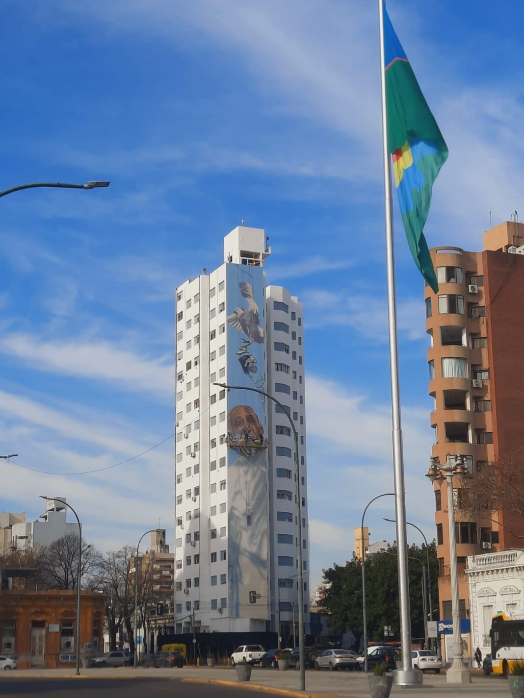Vista del mural del Papa Francisco en La Plata con la bandera de la Provincia de Buenos Aires en primer plano