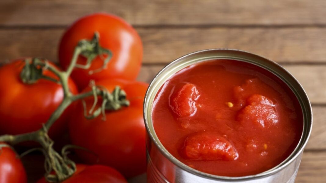Lata de tomate triturado rodeada de tomates frescos, afectada por alerta de ANMAT