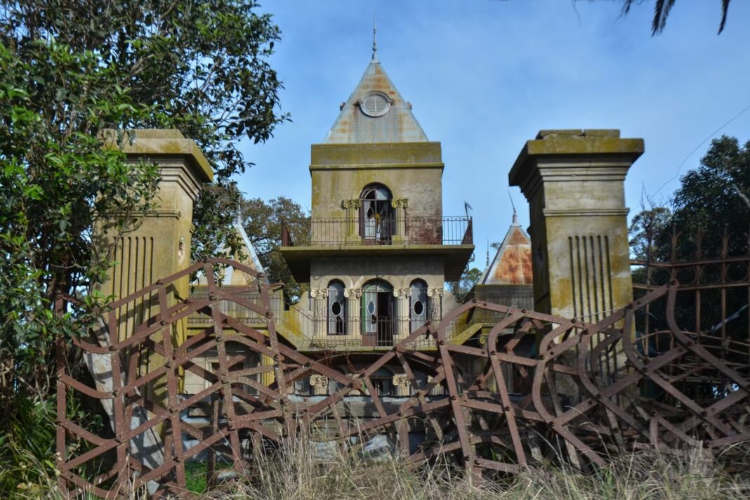 Fachada del castillo abandonado de Coronel Dorrego, rodeado de vegetación y una reja oxidada.