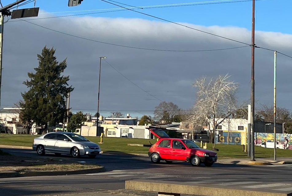 Cielo parcialmente nublado en una esquina de La Plata, con tránsito leve y semáforo en rojo.