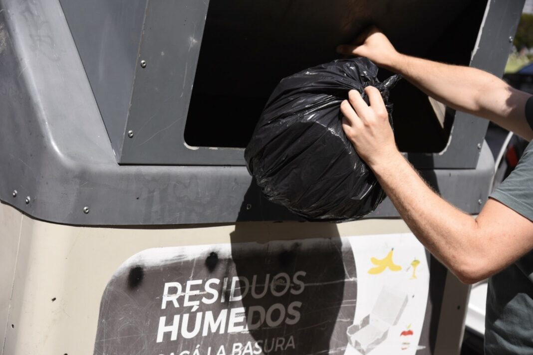 Persona depositando una bolsa de basura en contenedor de residuos húmedos en La Plata
