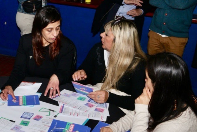 Mujeres participan en una actividad sobre género y diversidad en La Plata, trabajando con folletos informativos en una mesa grupal.