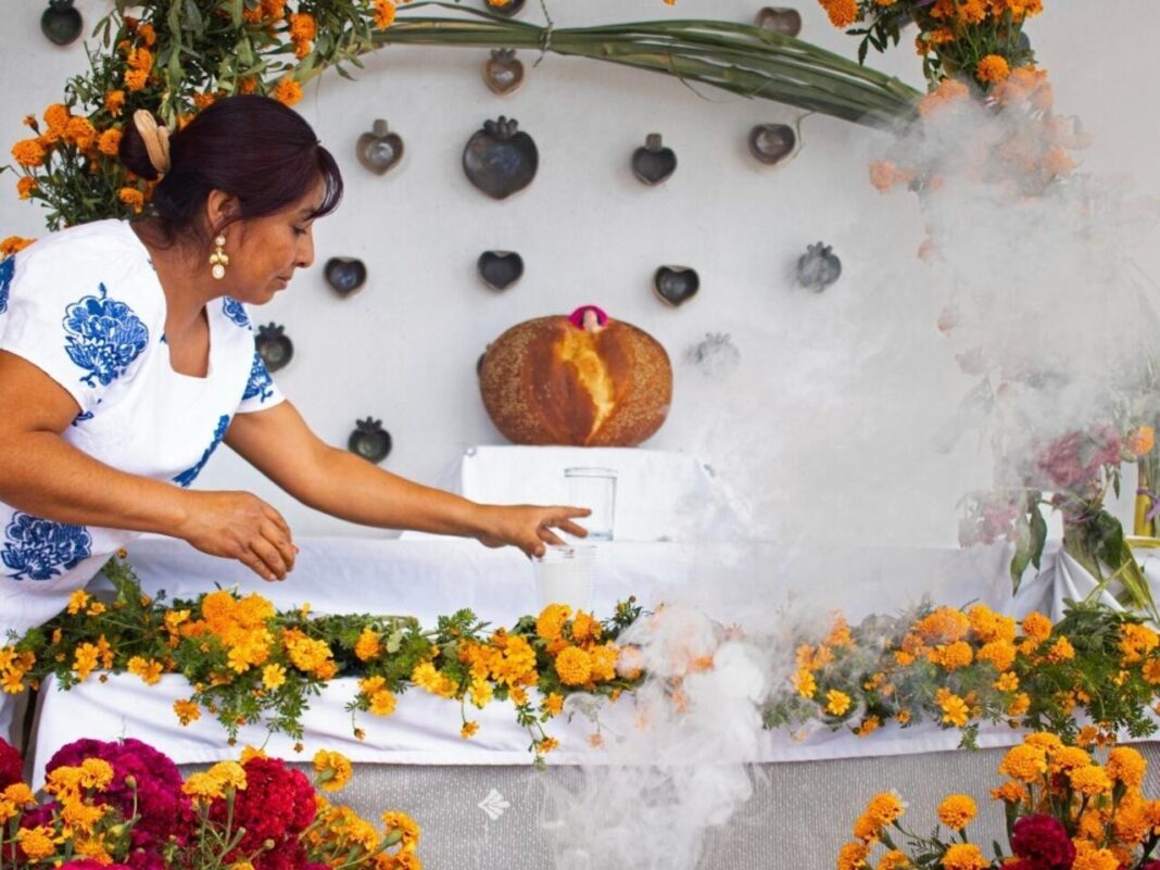 Mujer preparando un altar de ofrendas con flores de cempasúchil y humo, representando las tradiciones locales en contraste con Halloween.