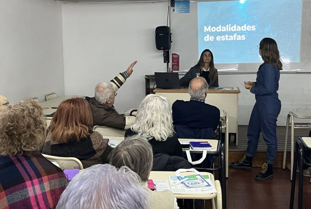 Guía Práctica contra Estafas: Capacitaciones Municipales en La Plata Capacitación del Municipio de La Plata sobre modalidades de estafas, mostrando a mujeres presentando material a un grupo de adultos mayores.