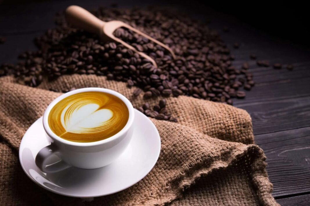 Taza de café con arte latte en forma de corazón sobre arpillera y granos de café