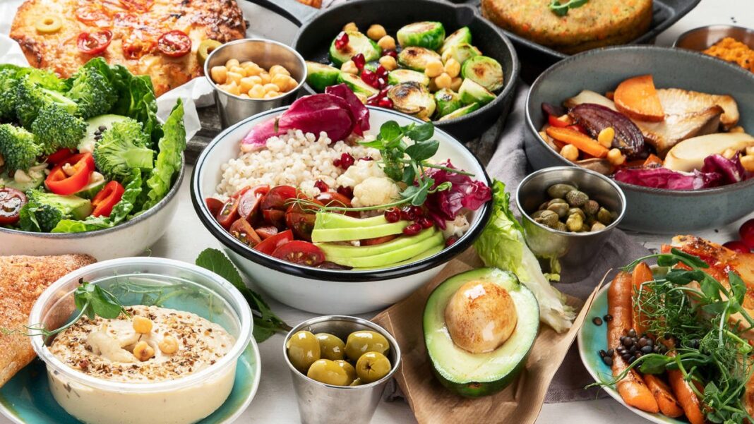 Vista cenital de un variado y vibrante plato de comida saludable de verano, mostrando ensaladas, bowls de granos, vegetales asados y dips, ideal para recetas frescas y sin horno.