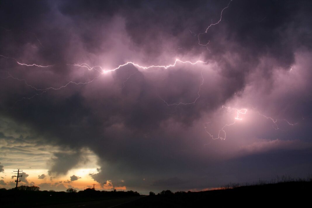 Fotografía dramática de múltiples rayos horizontales y ramificados iluminando nubes de tormenta oscuras sobre el paisaje silueteado de una carretera en el AMBA durante el atardecer, indicando la llegada de mal tiempo.