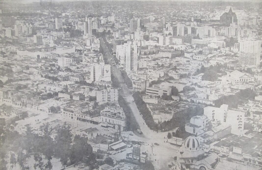 Fotografía aérea histórica en blanco y negro de La Plata, mostrando una avenida principal y el desarrollo urbano con edificios antiguos y modernos, incluyendo una cúpula prominente, celebrando los 143 años de la ciudad.