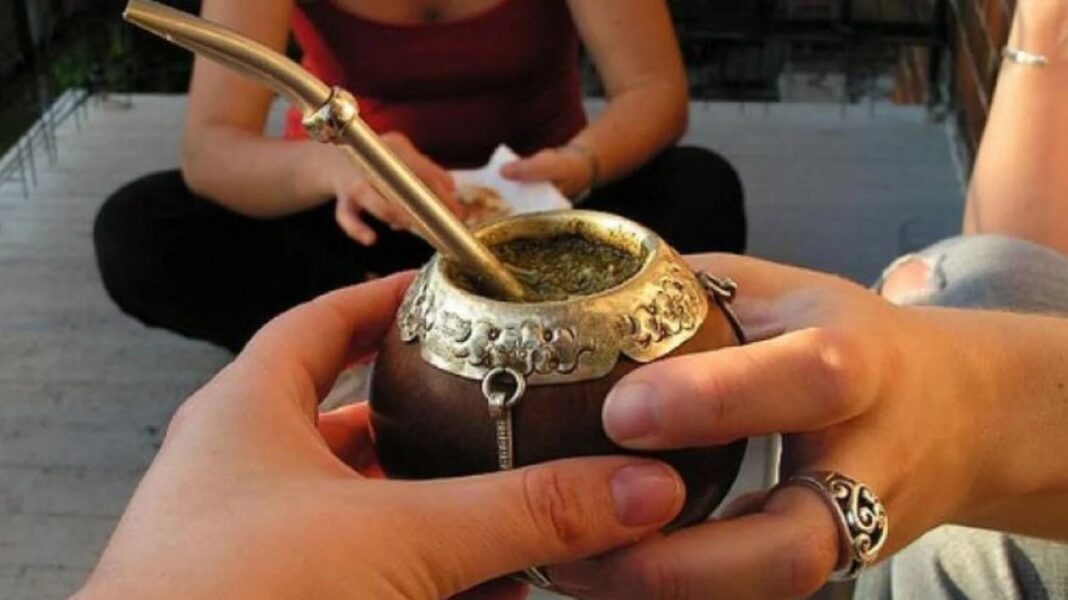 Primer plano de dos personas compartiendo un mate tradicional con decoración de metal, sostenido por sus manos, celebrando el Día del Mate en la región del Río de la Plata.