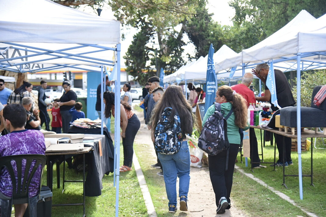 Feria de servicios comunitarios al aire libre en City Bell con carpas blancas, donde los vecinos se acercan a realizar trámites de DNI, cargar la SUBE y vacunarse durante la semana.