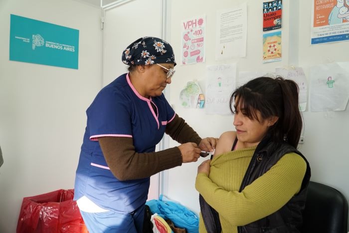 Trabajadora de la salud administrando una vacuna en el brazo a una mujer en un vacunatorio de la Provincia de Buenos Aires, destacando la actividad sanitaria bonaerense.