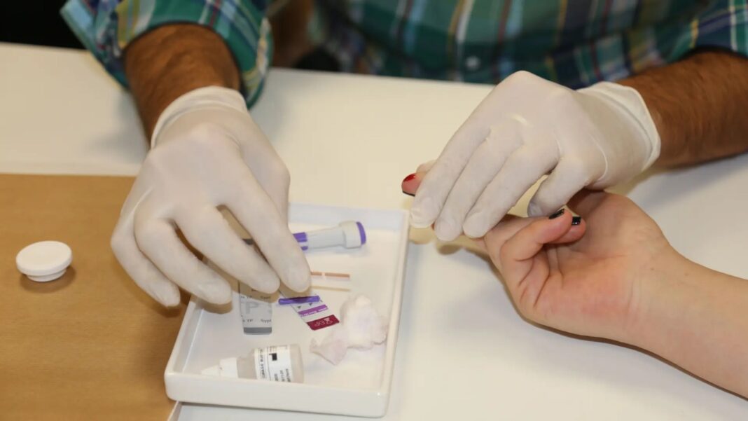 Preparación de un kit de test rápido de sífilis: persona con guantes tomando una muestra de sangre de un dedo para el diagnóstico de la enfermedad en Argentina.
