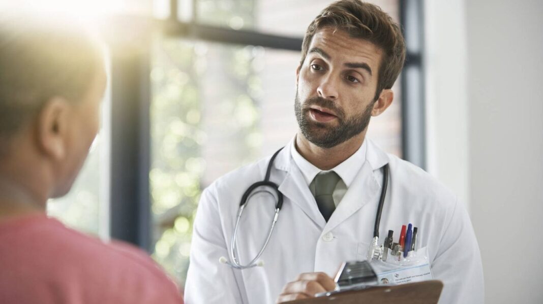 Médico con bata blanca y estetoscopio atendiendo atentamente a un paciente en el Día del Médico, 3 de diciembre.