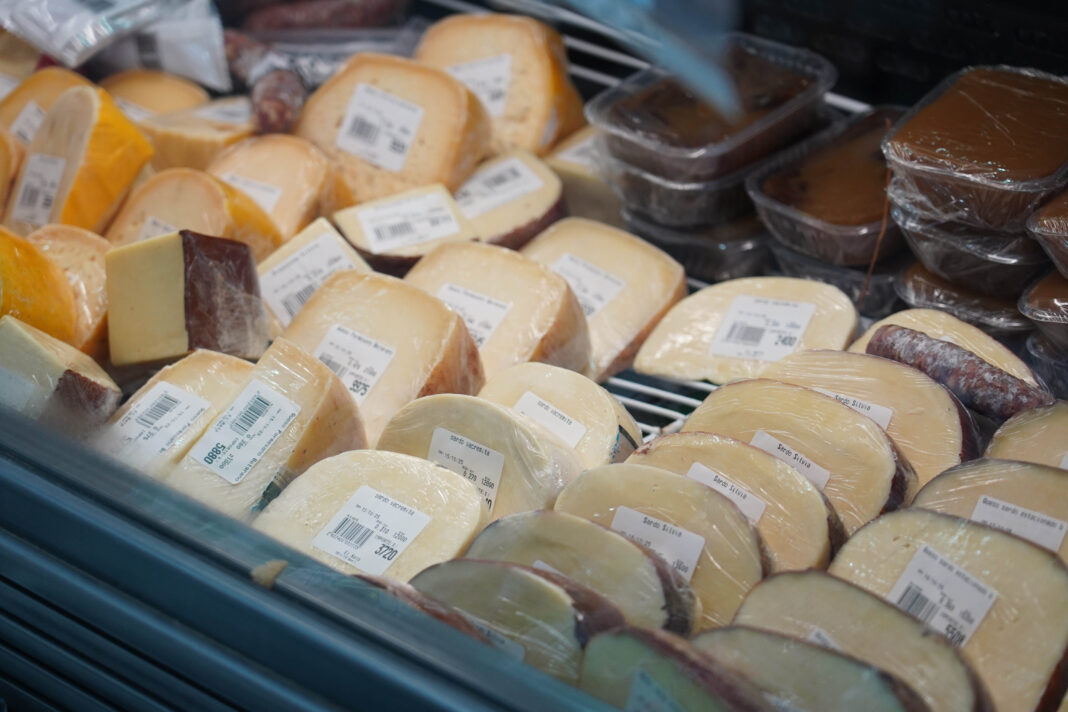 Primer plano de una vitrina refrigerada con variedad de quesos en el Mercado Bonaerense Fijo de La Plata, destacando las nuevas ofertas de precios.