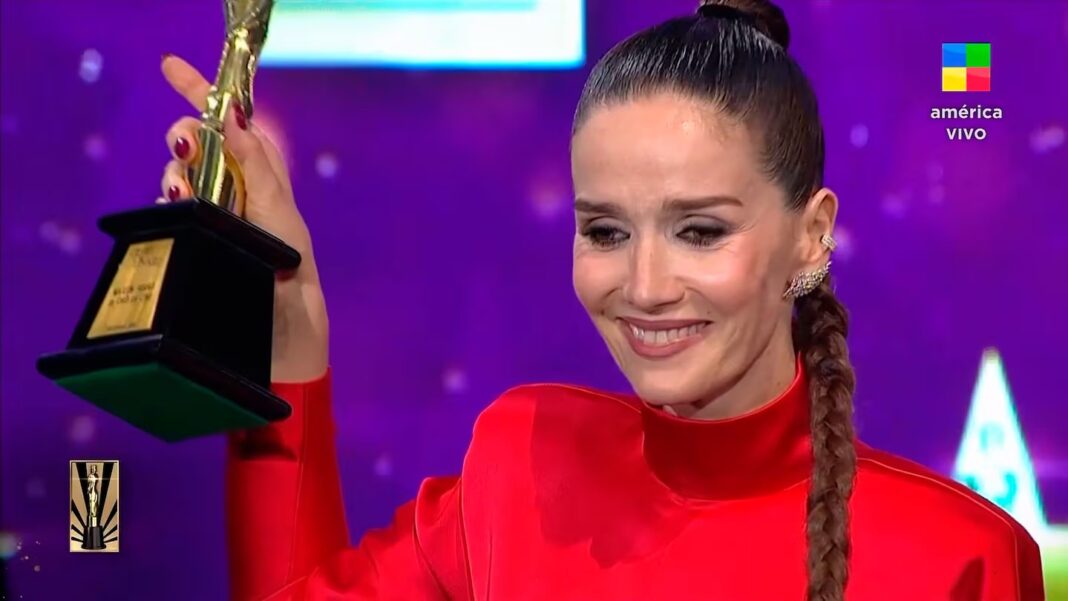 Natalia Oreiro sonriendo con un vestido rojo mientras sostiene el trofeo Martín Fierro 2025, celebrando su victoria antes del galardón de 