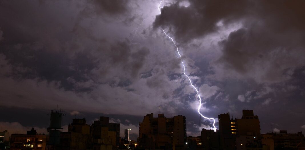 Rayo impactando durante una fuerte tormenta nocturna sobre el horizonte de una ciudad de la Provincia de Buenos Aires, ilustrando el pronóstico de descenso térmico.