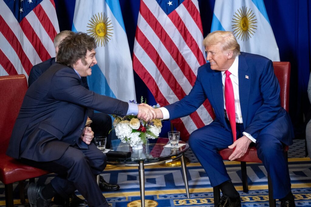 Javier Milei y Donald Trump se saludan durante una reunión oficial con banderas de Argentina y Estados Unidos de fondo.