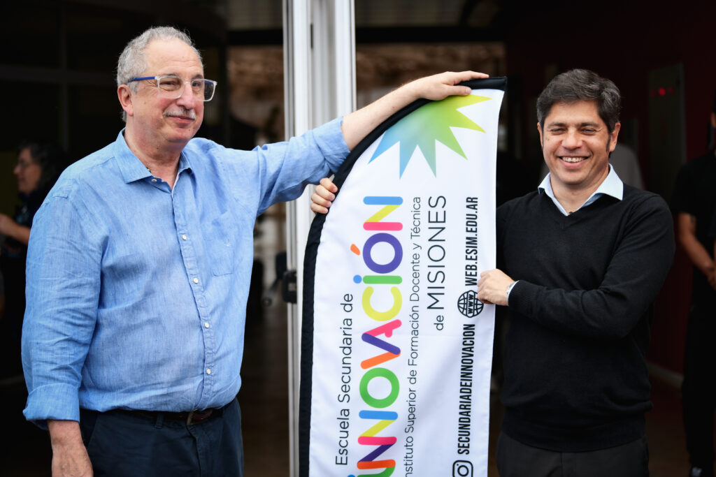 hugo passalacqua y axel kicillof posan al lado de un cartel durante una recorrida por una escuela de misiones